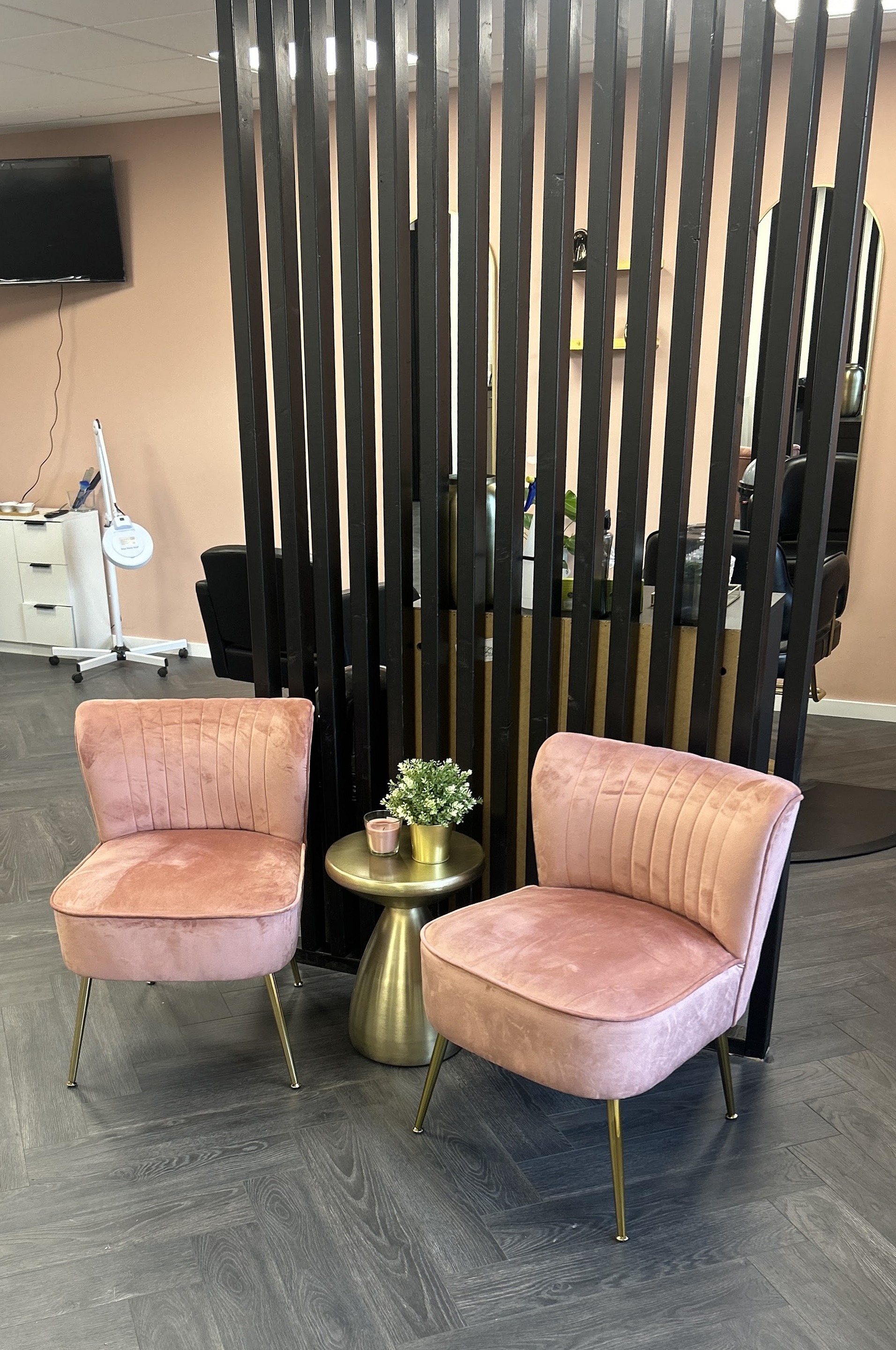 De wachthoek van de salon: twee roze fluwelen stoelen bij een goudkleurig tafeltje, met een zwarte lamellenwand erachter