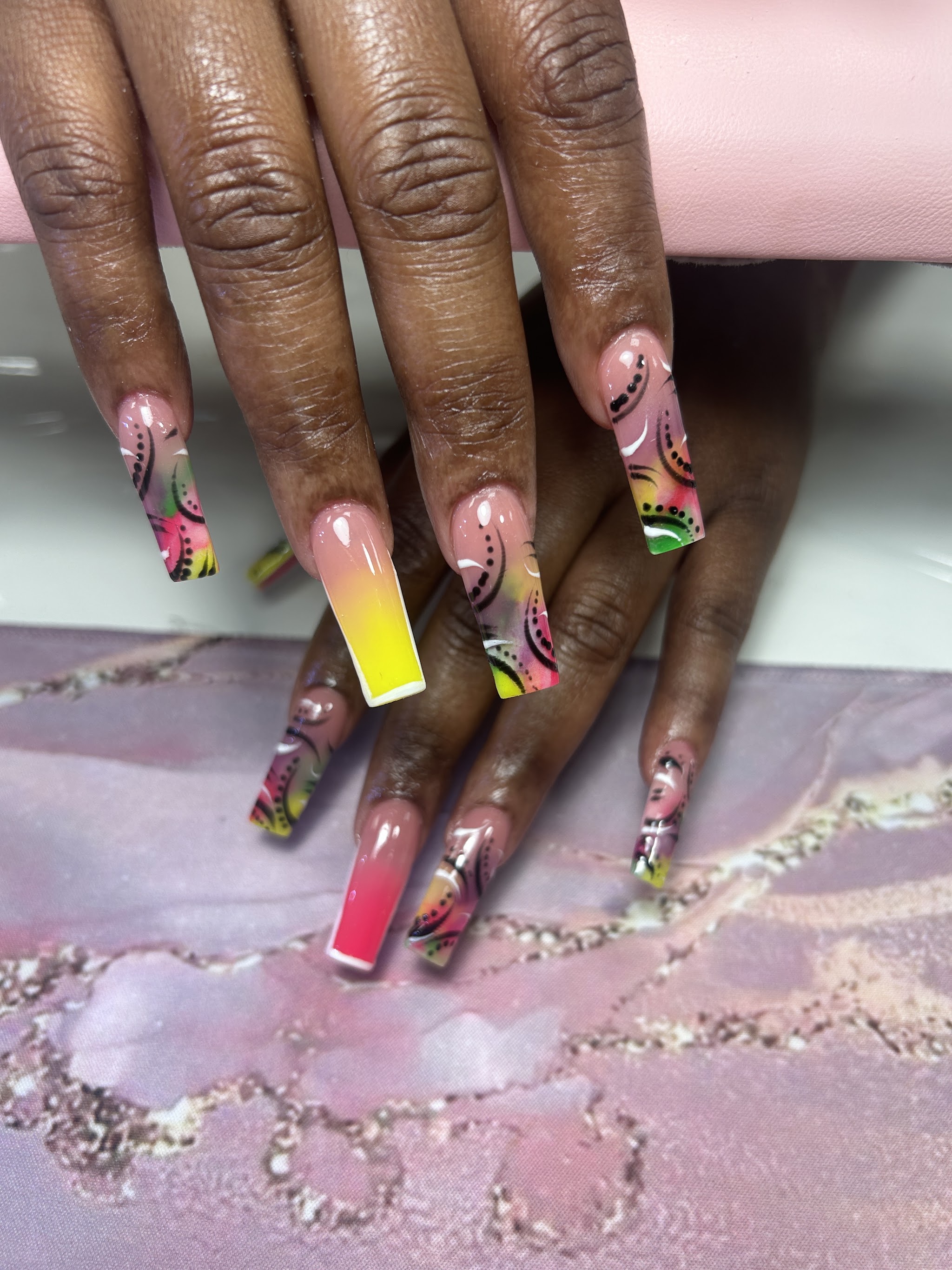Lange nagels met een roze naar gele ombré en kleurrijke nail art, op een marmeren mat