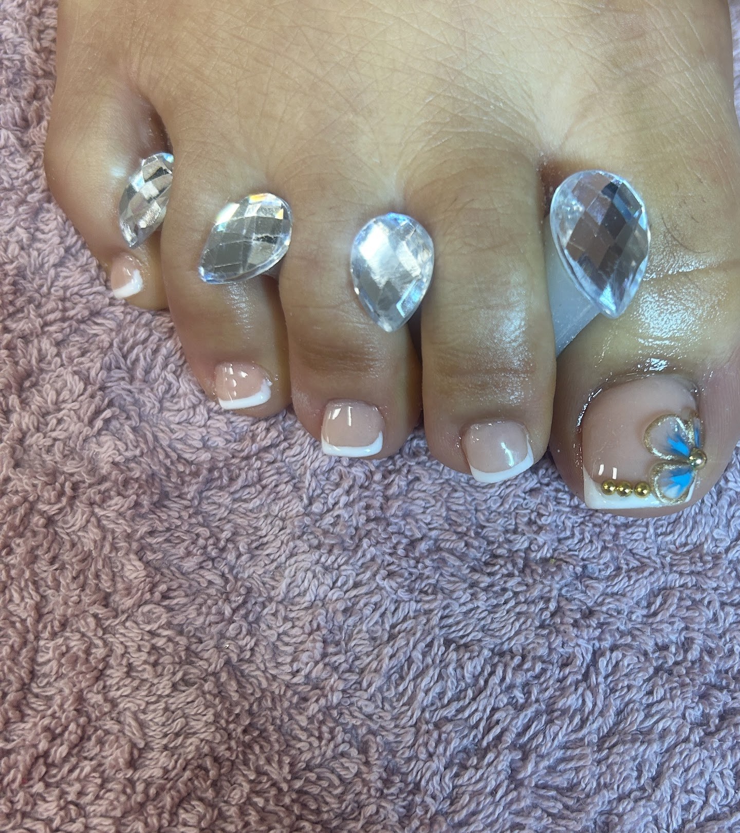 Teennagels met witte French tips, op de grote teen een bloemetje met steentjes, en sierstenen tussen de tenen