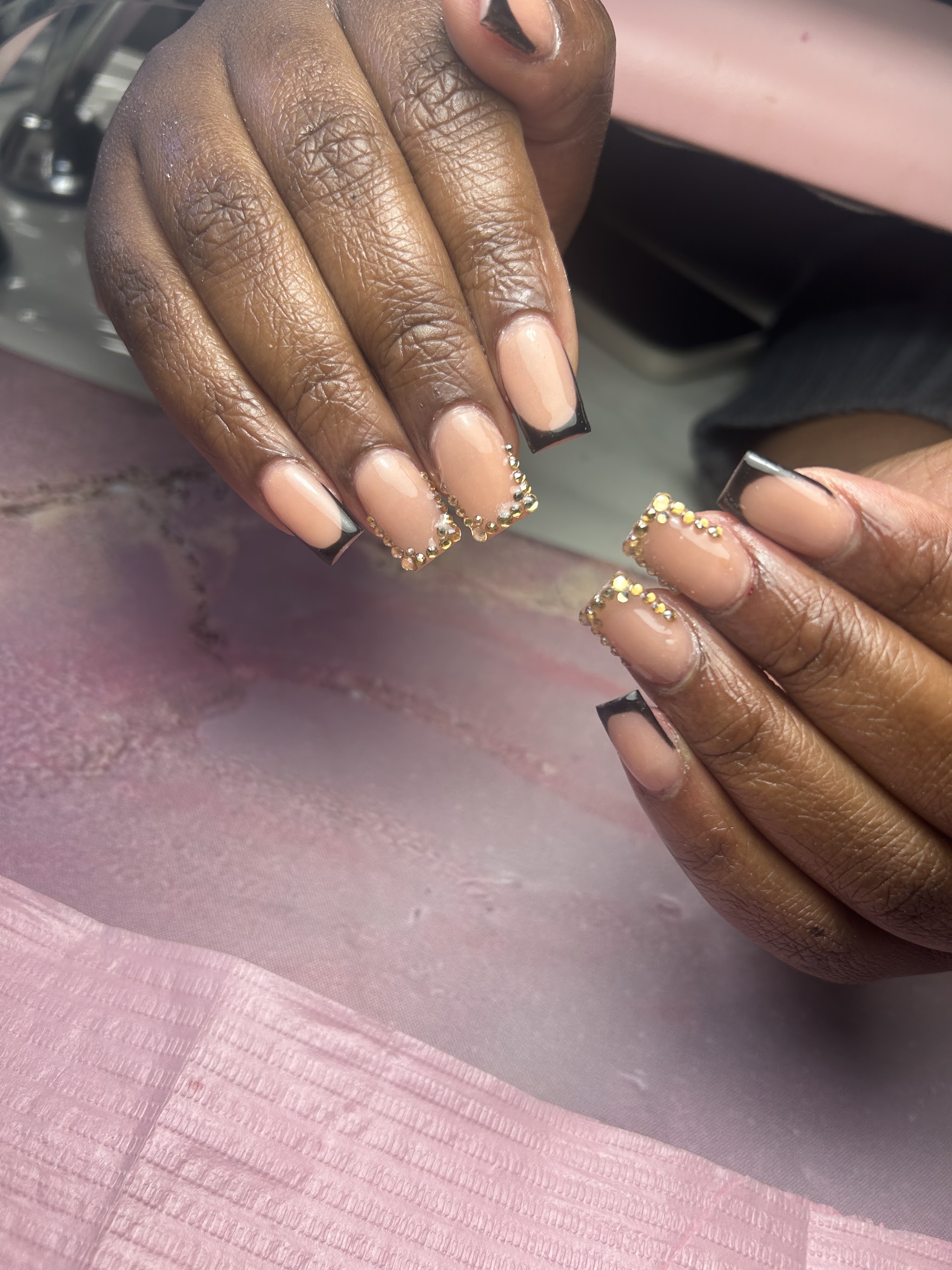 Naturel nagels met zwarte tips en gouden studs, op een roze mat